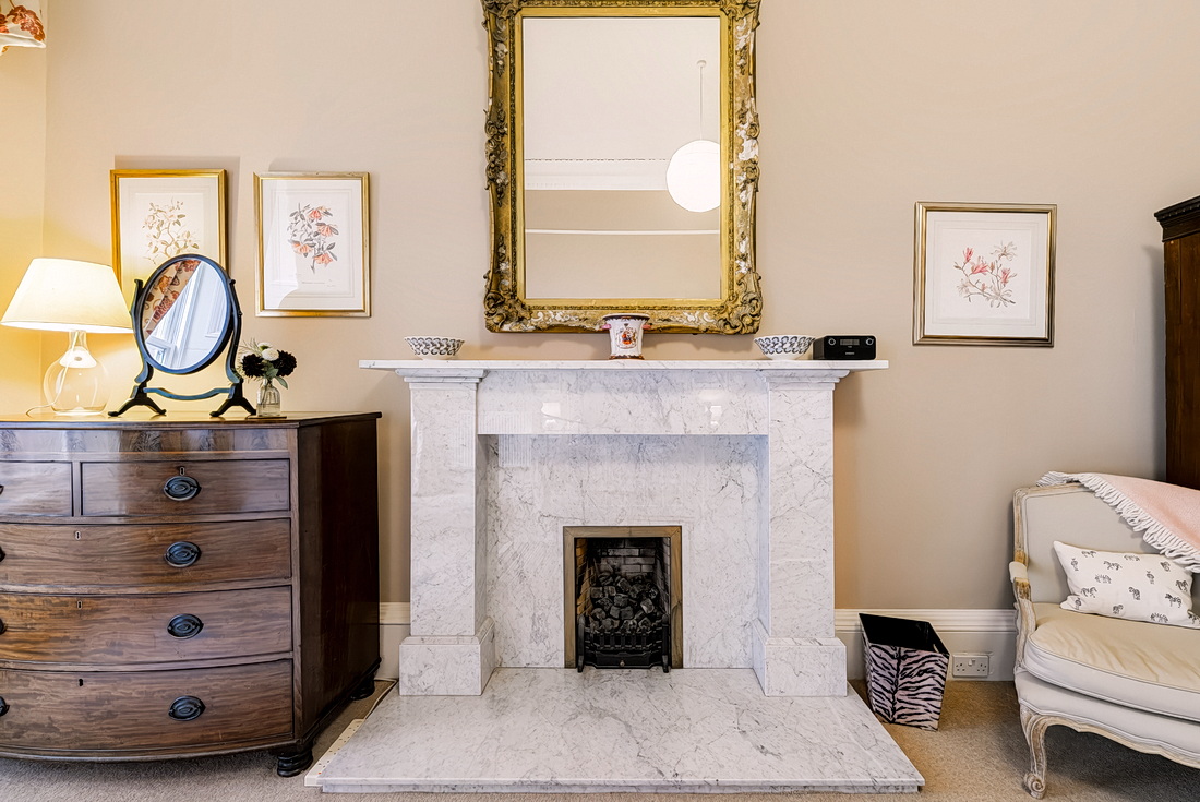 Master bedroom marble fireplace with gilt mirror and antique chest of drawers