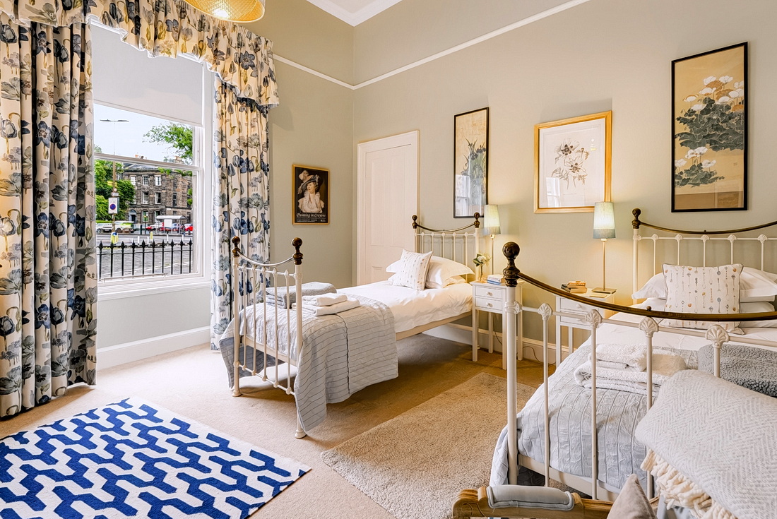 Twin bedroom with two cast-iron style single beds and a tall window over the public gardens