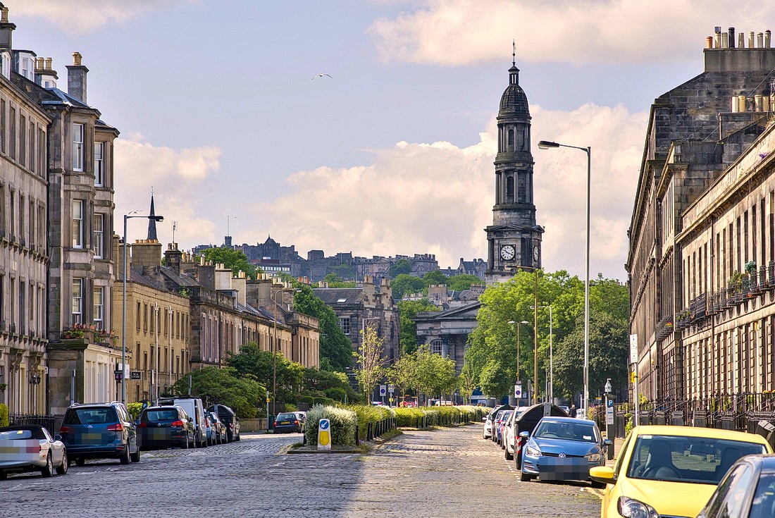 A sunny view down the cobbled street towards the church spire, with Edinburgh Castle beyond