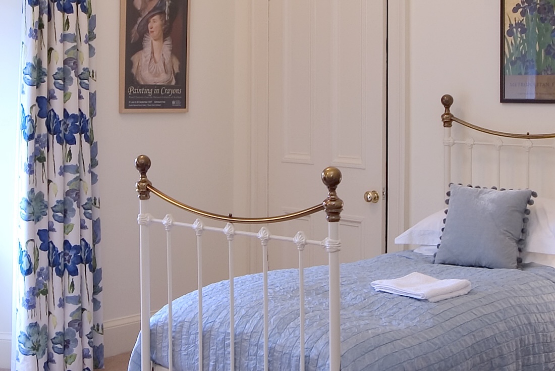 The twin room’s cast-iron bed with blue bedding and floral curtains